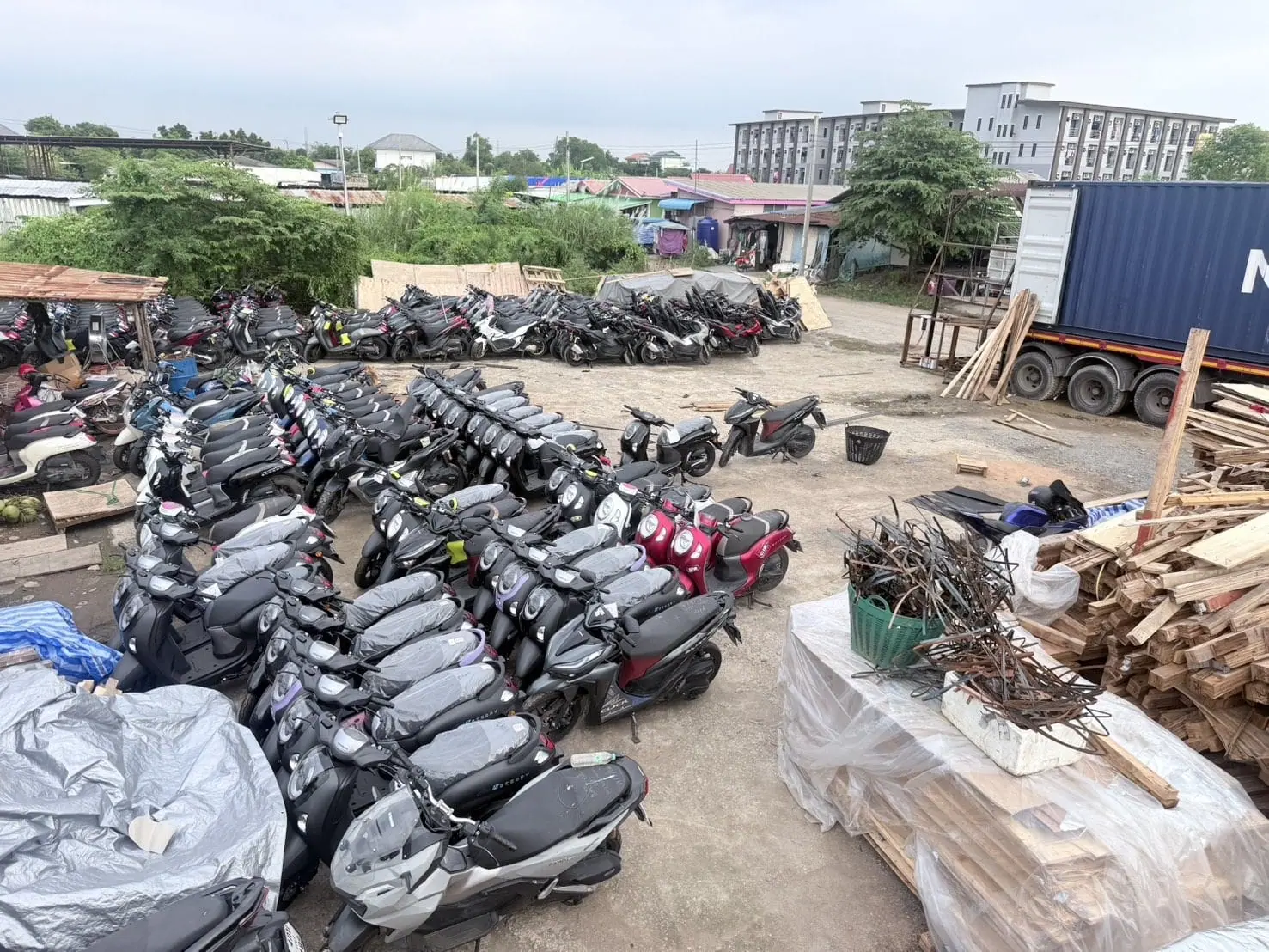 รถจักรยานยนต์จำนวนมากจัดเรียงเป็นแถวในลานข้างรถบรรทุกตู้ Container